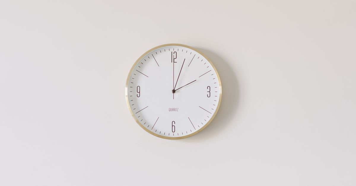 Minimalist round wall clock with gold rim and white face on a white wall.